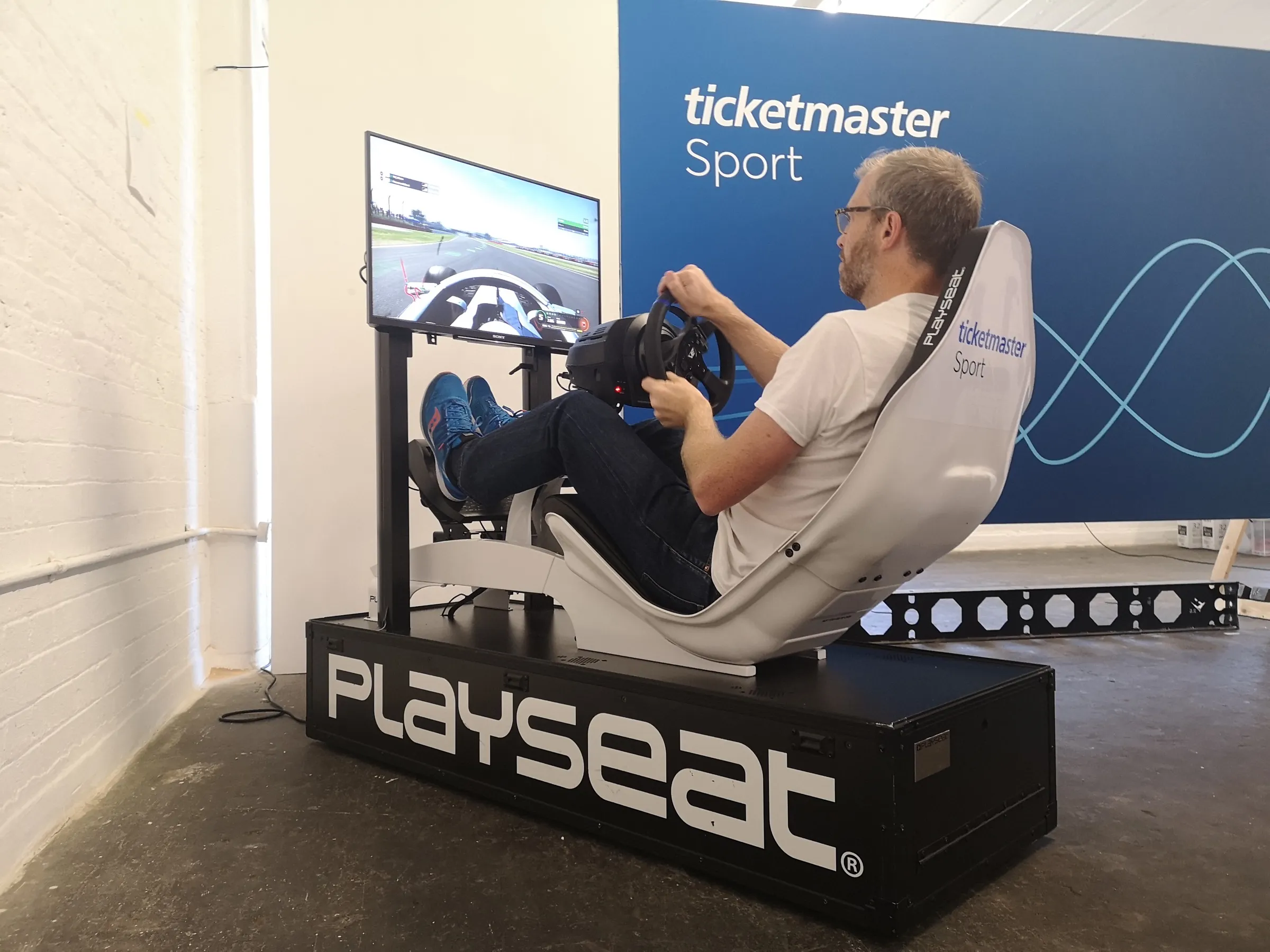Guest racing a white simulator with a branded seat in front of a branded backdrop