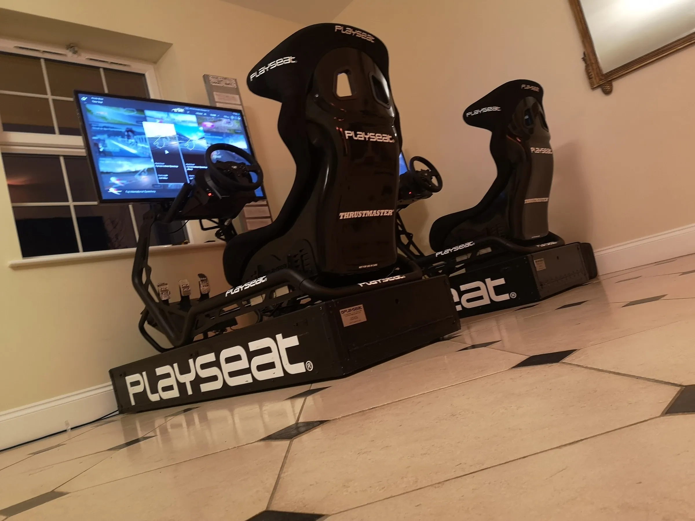 Two black racing simulators side by side in a hotel function room with a screen on a stand