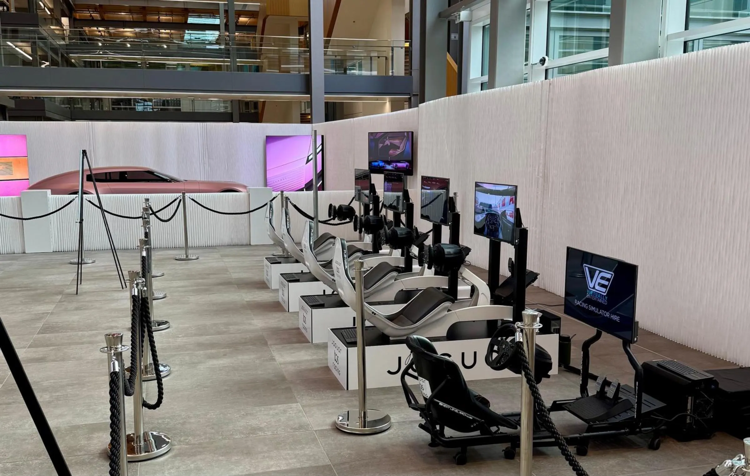 Row of racing simulators with Jaguar and Virtually Entertained branding in a building atrium