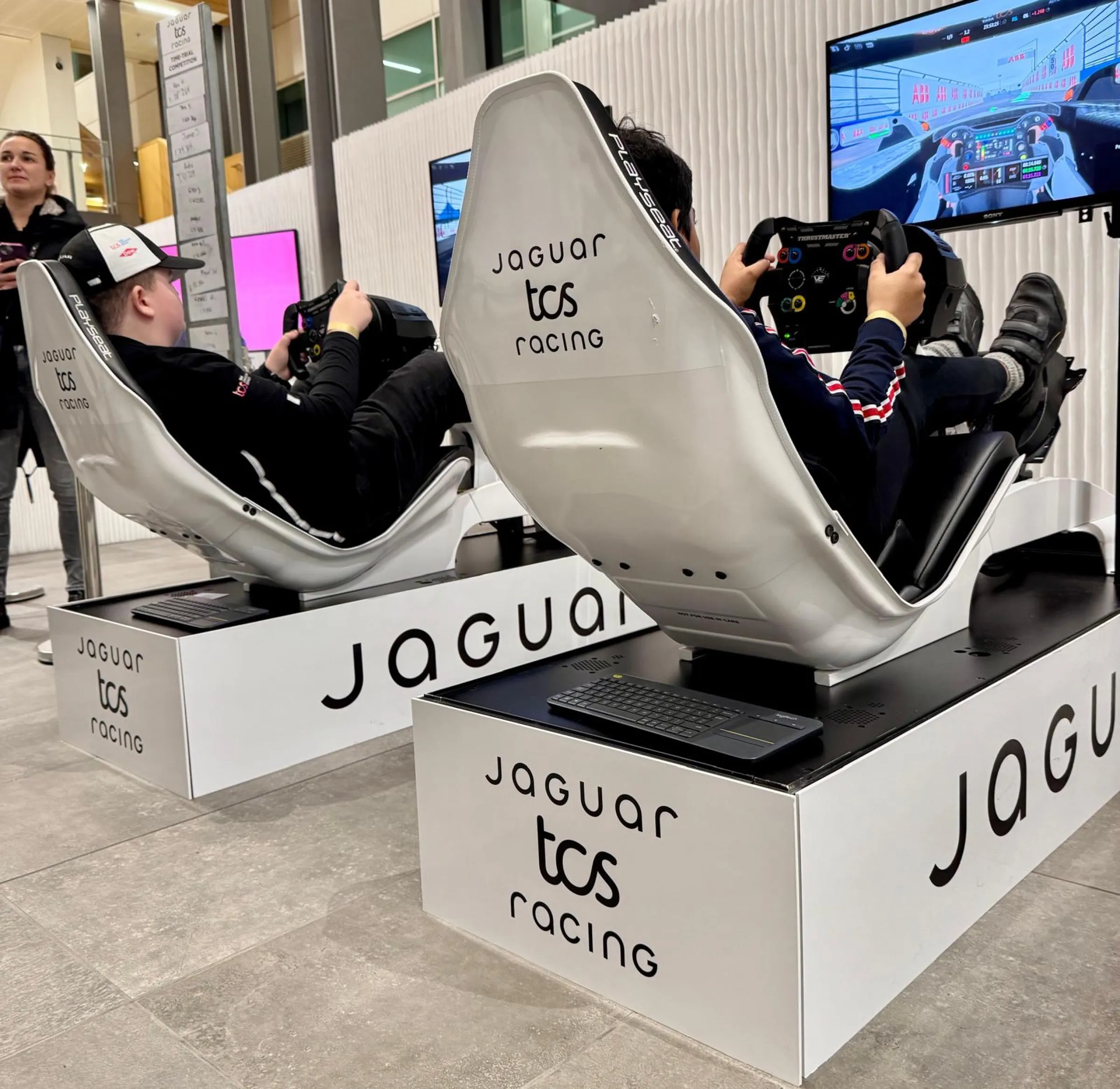 Two drivers racing branded Jaguar TCS Racing simulators side by side in a time trial