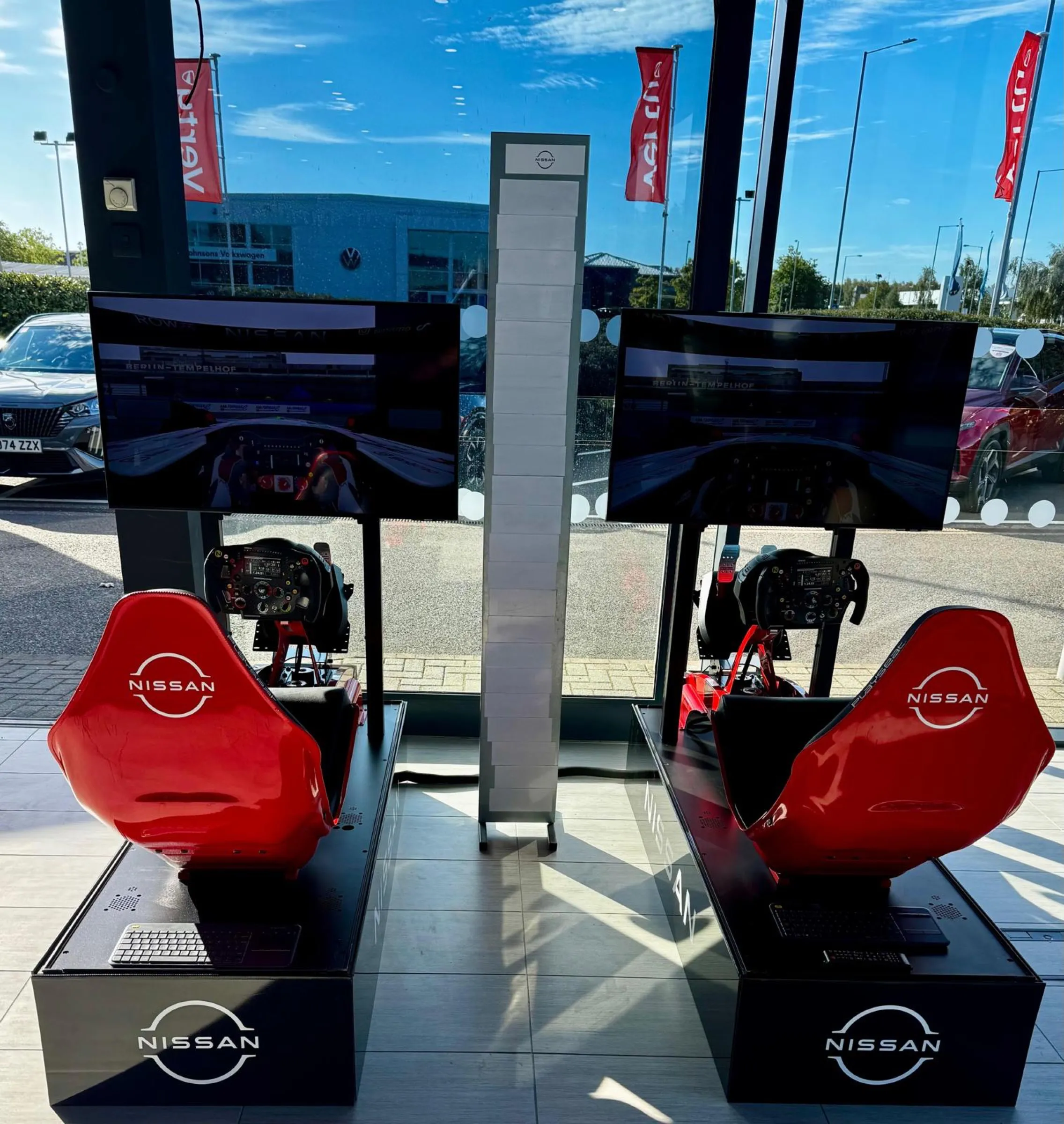 Pair of full-wrap red Nissan racing simulators standing on a dealership showroom floor